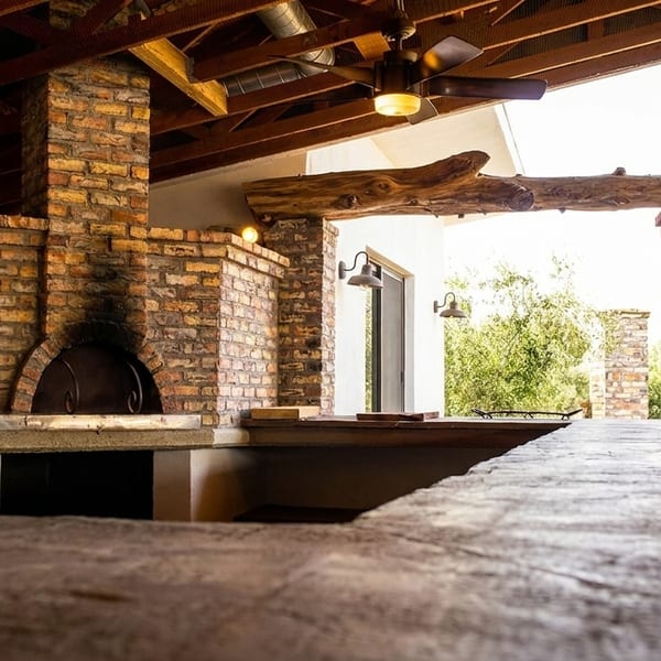 Outdoor kitchen with a brick pizza oven, wooden beams, and a concrete countertop under a patio.