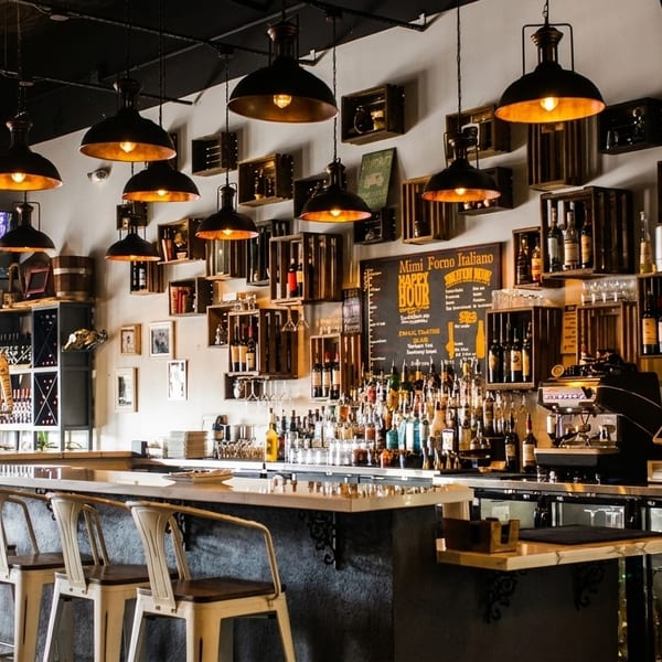 A well-lit bar area with stools, bottles, and a chalkboard menu at Mimi Forno Italiano.