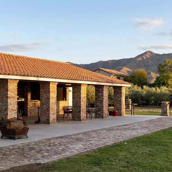 Outdoor patio with brick columns and tiled roof, leading to a grassy area with mountains in the background.