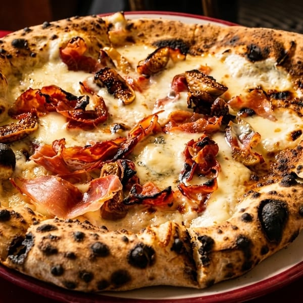 Neapolitan pizza with prosciutto, figs, and melted cheese on a red plate.