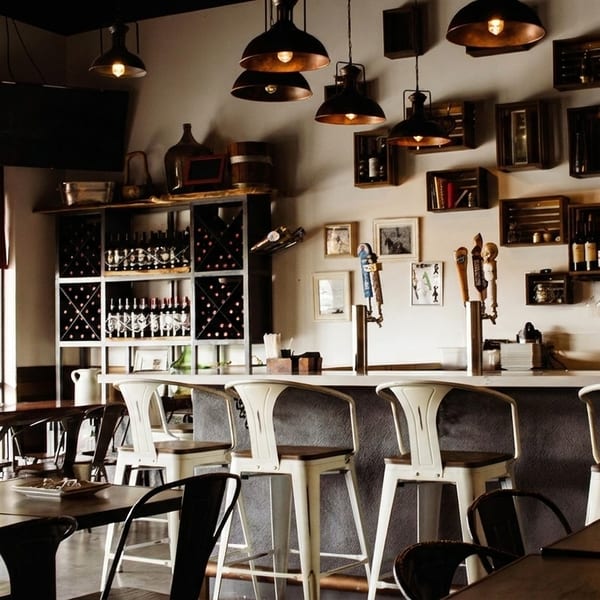 A restaurant interior with a bar, high stools, dining tables, and wine racks.