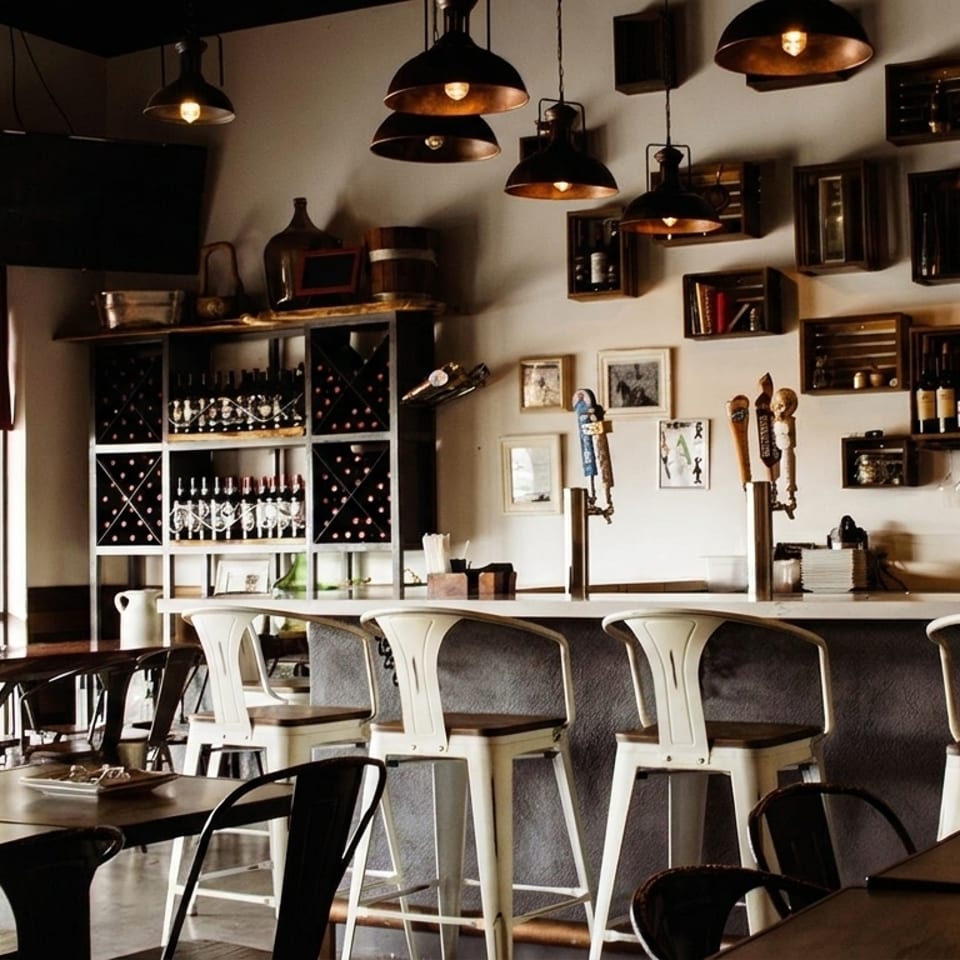 A restaurant interior with a bar, high stools, dining tables, and wine racks.