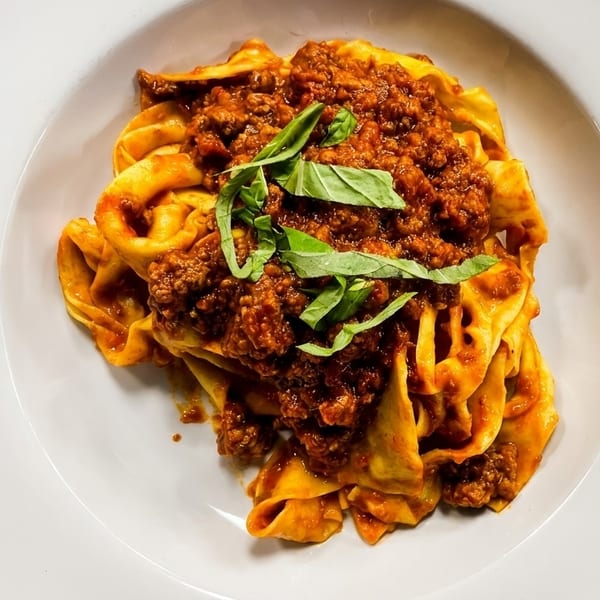 Pappardelle pasta with rich bolognese sauce and fresh basil on a white plate.